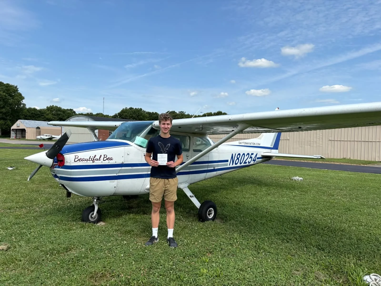 New private pilot Devin Schwartz holding his certificate beside a Cessna 172 in Dayton
